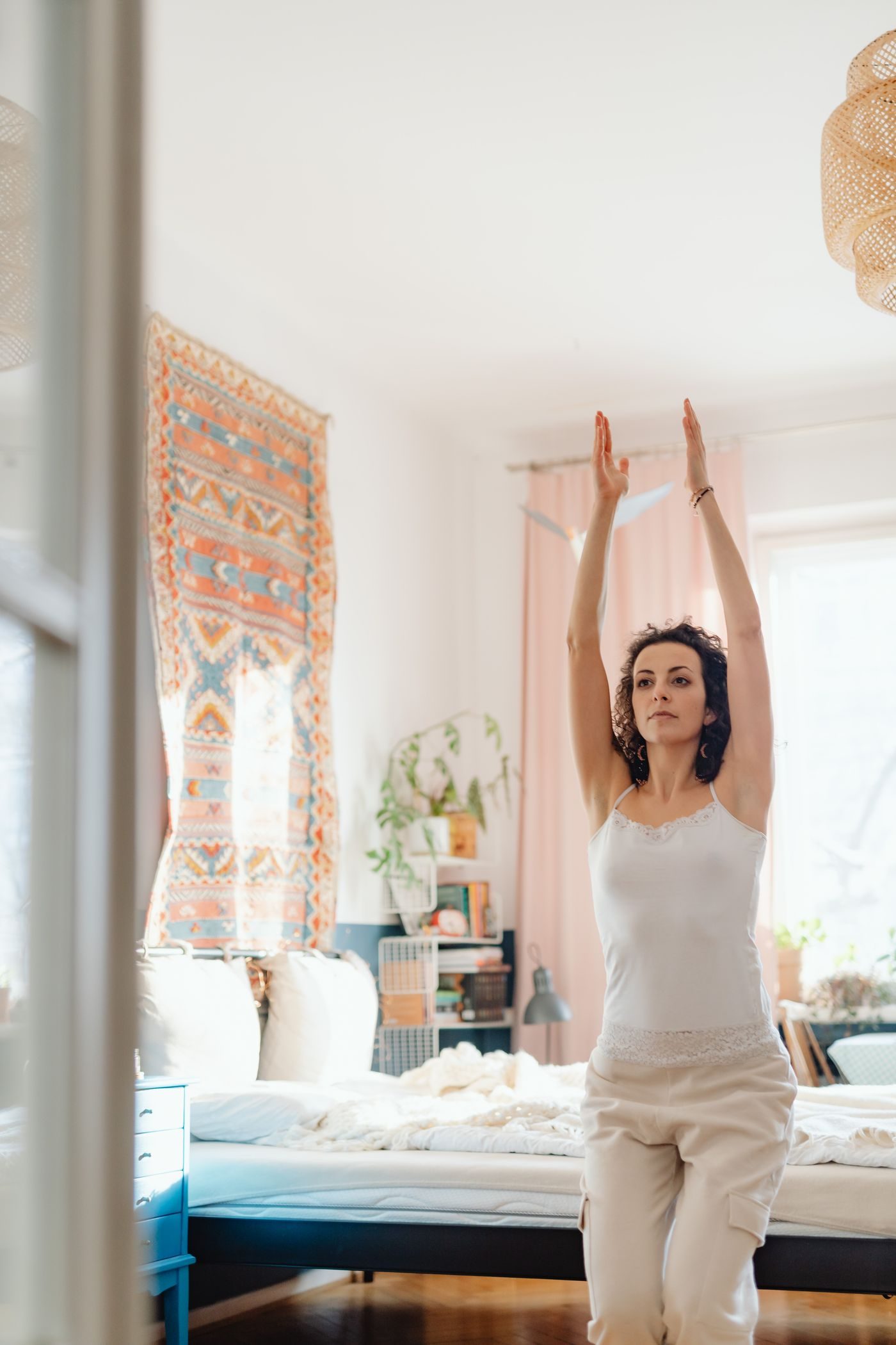 Woman stretching in a sunlit bedroom before her daily routine